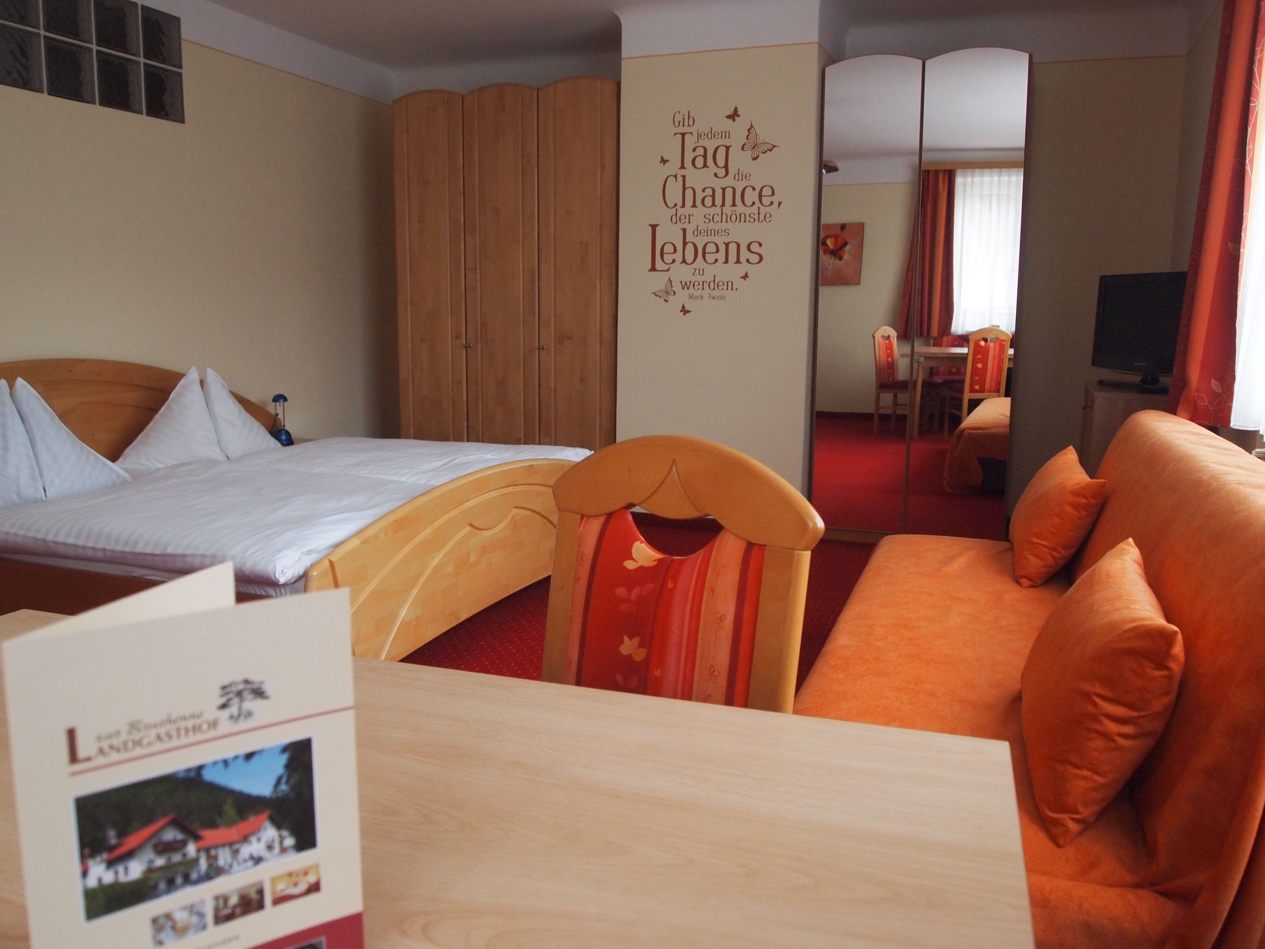 A cozy hotel room with a double bed, a sofa, a table and a wardrobe. There is a motivational slogan on the wall.