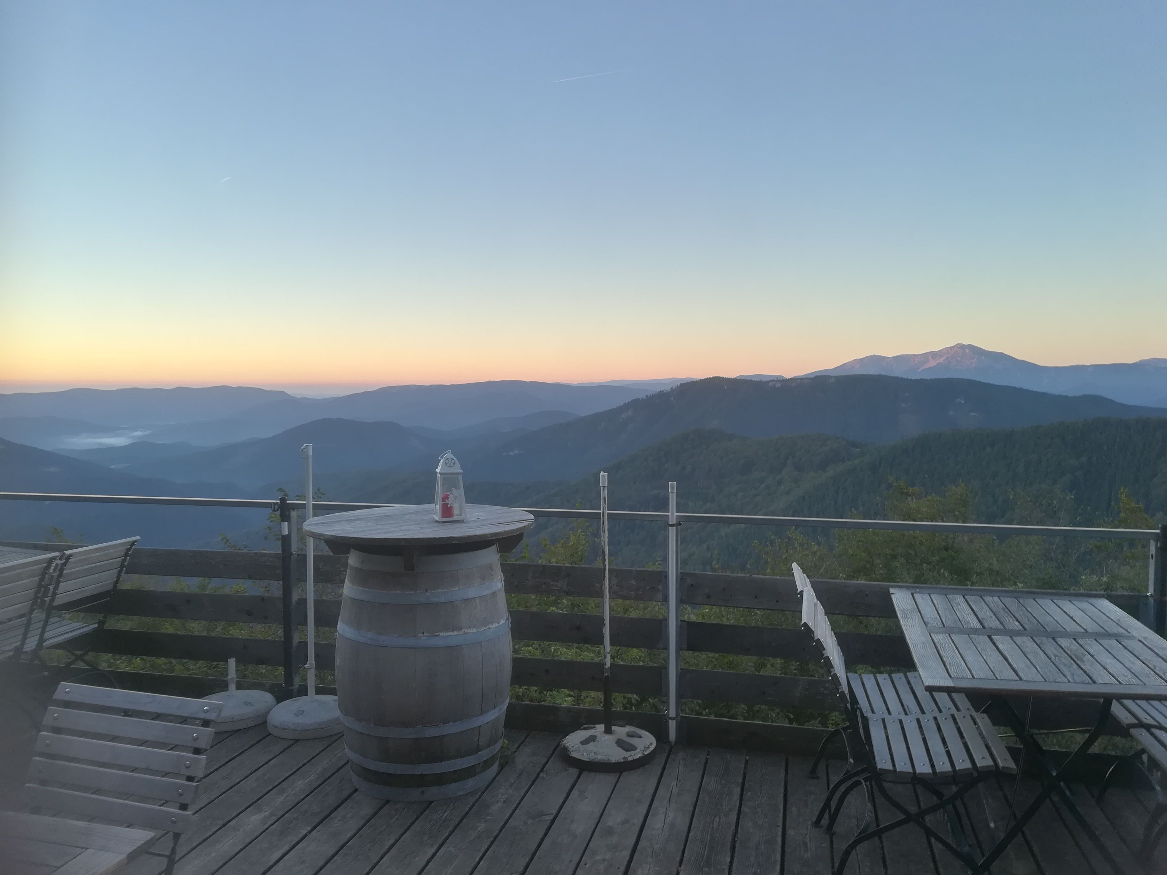 Terrace with wooden furniture and mountain views at sunrise.