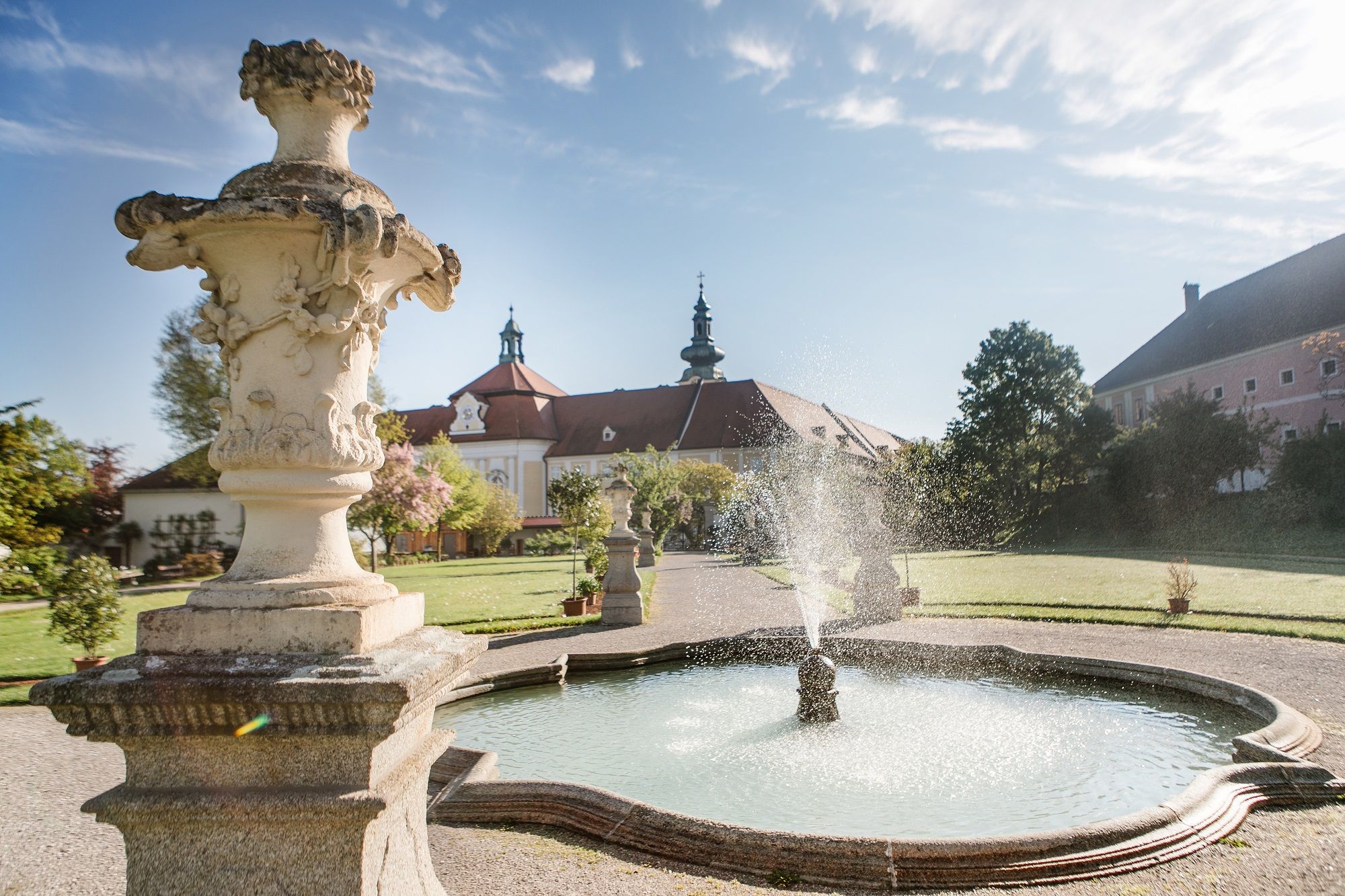 Fountain in the garden of Seitenstetten Abbey with baroque architecture in the background.
