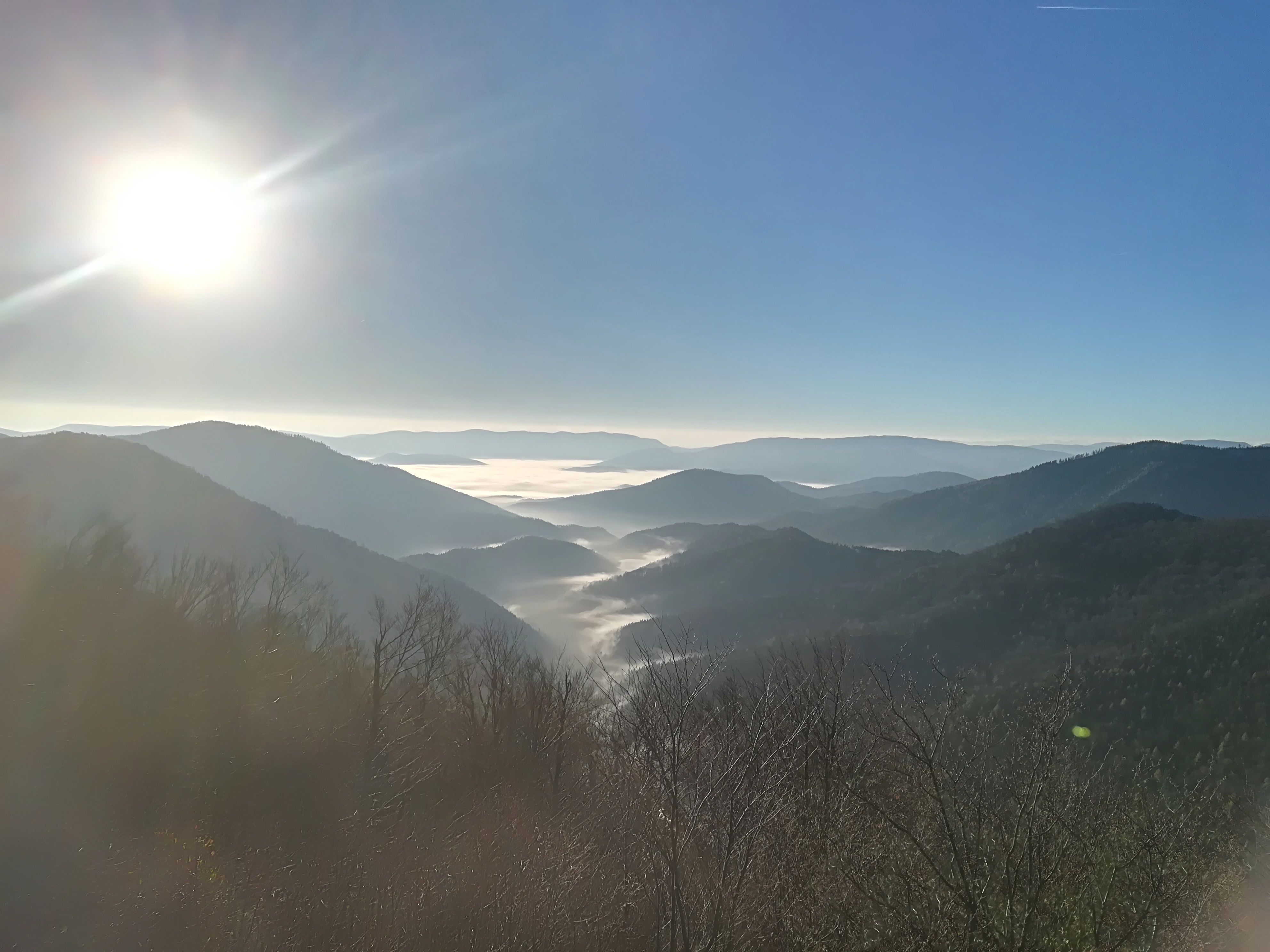 View from a mountain of mist-covered valleys and hills under a bright blue sky with sunshine.