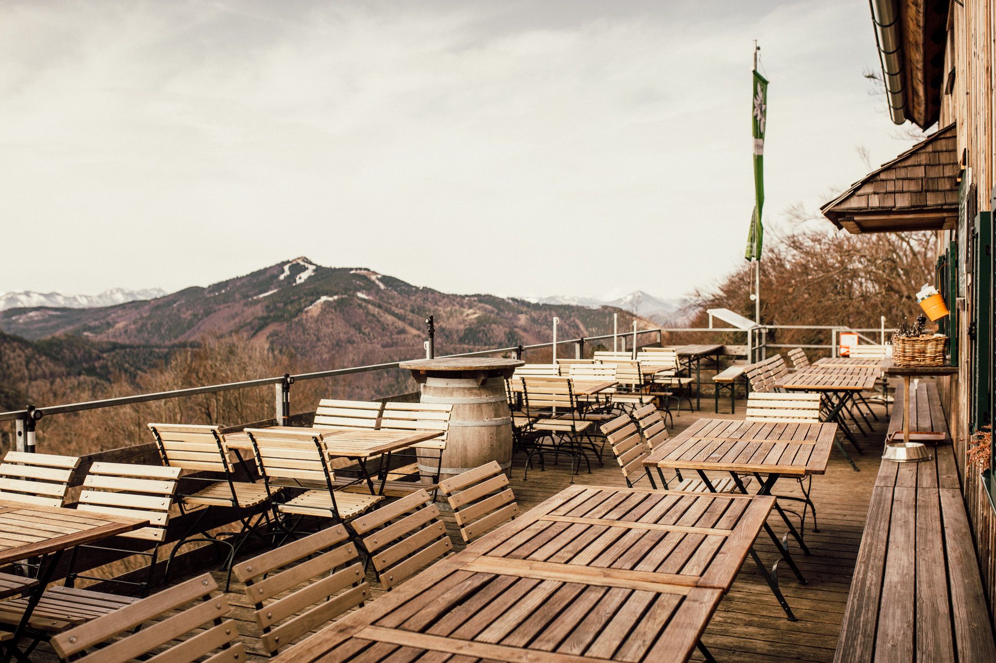 Empty terrace with wooden tables and chairs, mountain landscape in the background.