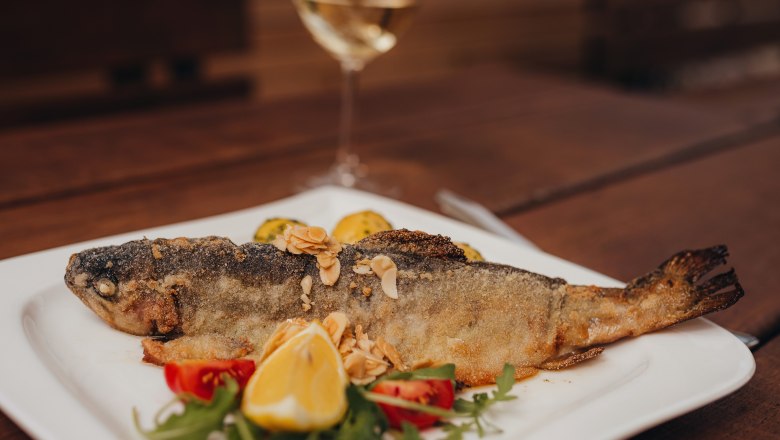 Fried trout with almond butter on a plate, garnished with lemon and vegetables.