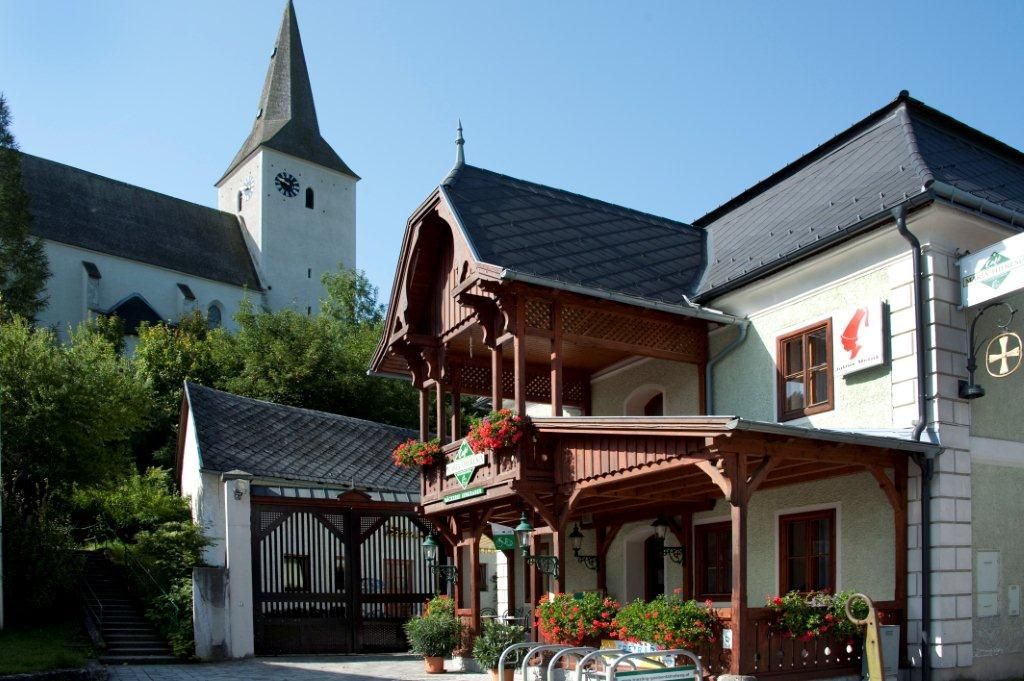 A traditional building with a wooden balcony and floral decorations, next to a church with a tower.