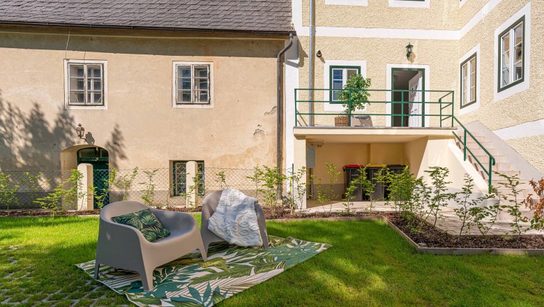 Garden with seating in front of an old building with a yellow façade and green window frames.