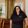 A woman with glasses stands in a cozy inn with stone walls and curtains.