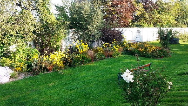 A well-tended garden with a green lawn, colorful flowerbeds and a white wall in the background.