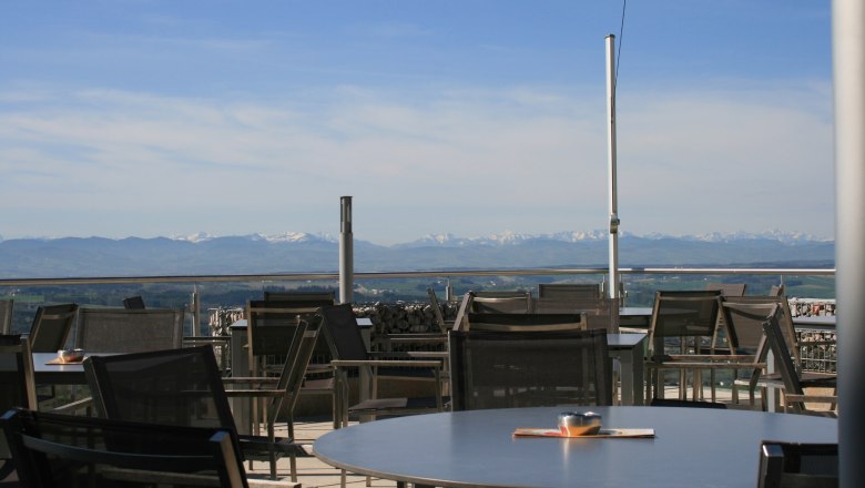 Terrace with tables and chairs, Alpine panorama in the background.