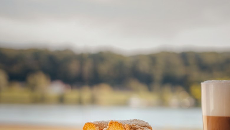 Piece of cake with strawberries and latte macchiato in front of a blurred landscape.