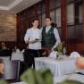 A female chef and a man in traditional dress stand smiling in an elegant restaurant.