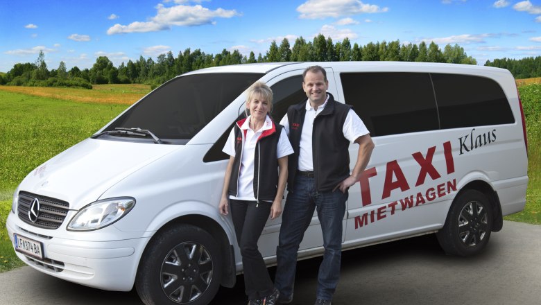 Two people are standing in front of a white Mercedes van labeled 'Taxi Mietwagen Klaus' on a rural road.