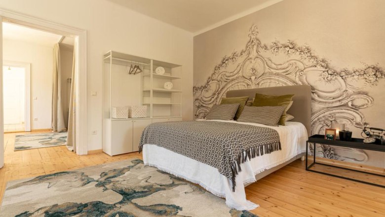 A stylishly furnished bedroom with a large bed, decorative cushions, a rug and an artistic wall design.