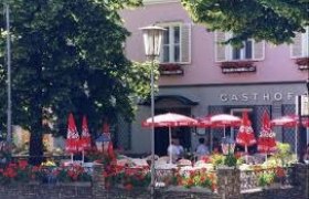 Exterior view of an inn with terrace, red parasols and floral decorations.