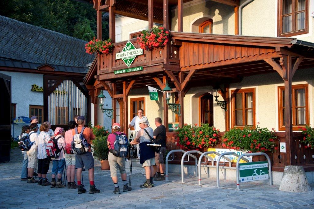 A group of hikers stands in front of the Café Maria Theresia with its wooden veranda and floral decorations.
