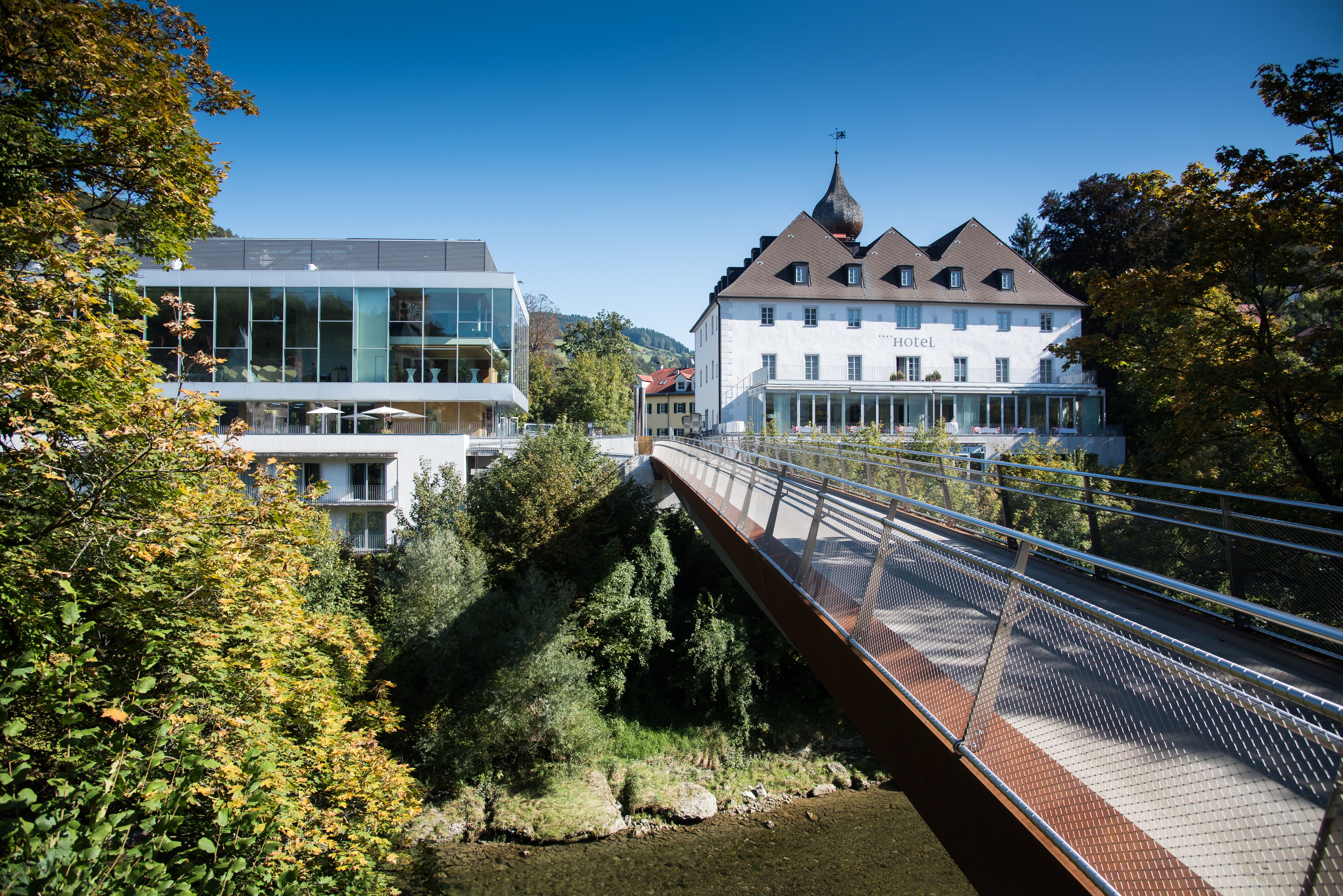 Modern and historic building with bridge in green surroundings.