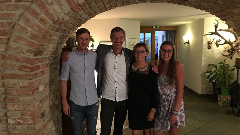 Four people stand smiling under a brick arch in a room with hunting trophies on the wall.