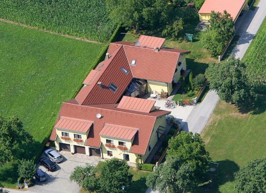Aerial view of a large house with red roofs, surrounded by green fields and trees.