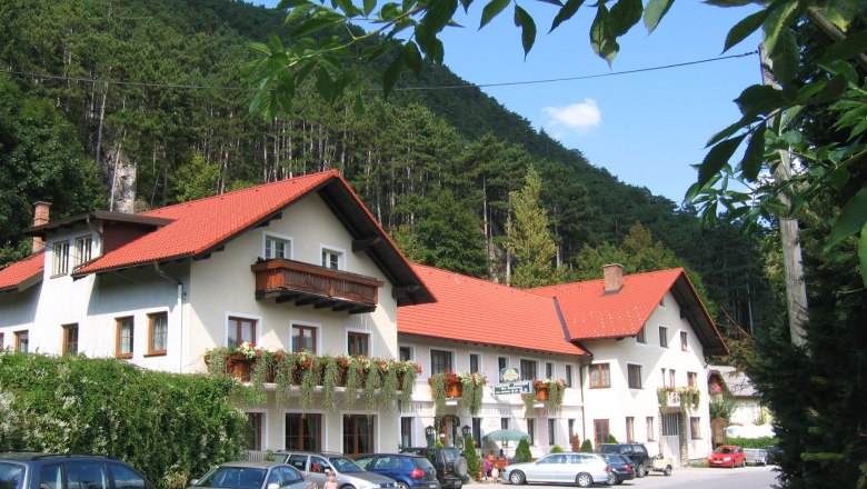 A traditional inn with red roofs and flower boxes, surrounded by woods and parked cars.