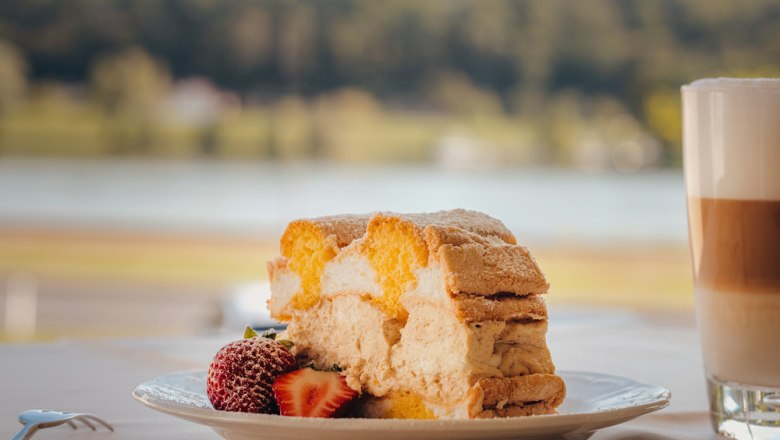 Piece of cake with strawberries and latte macchiato by the lakeside.