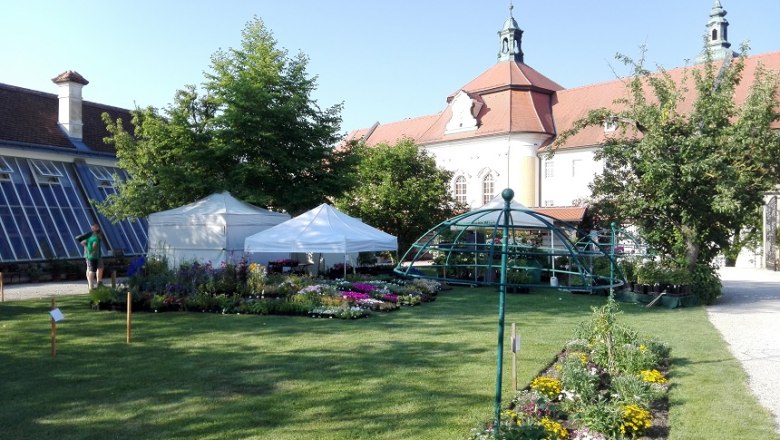 Garden with flower beds, white tents and historic building in the background.