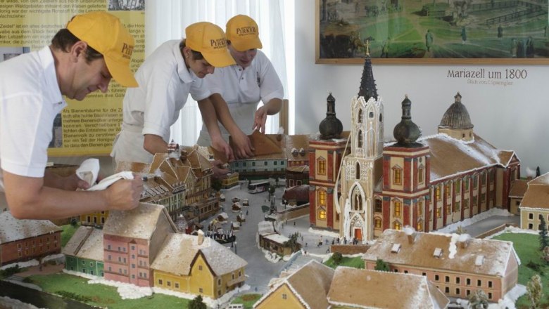 Three people decorate a gingerbread model of Mariazell around 1800.