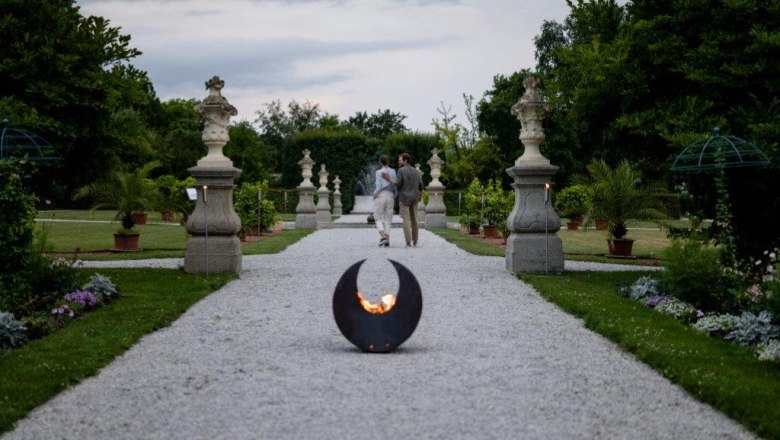 A gravel path in the historic courtyard garden of Seitenstetten Abbey with sculptures and plants, a fireplace in the foreground.