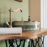A stylish bathroom with a decorative washbasin and a golden tap on a wooden washstand.