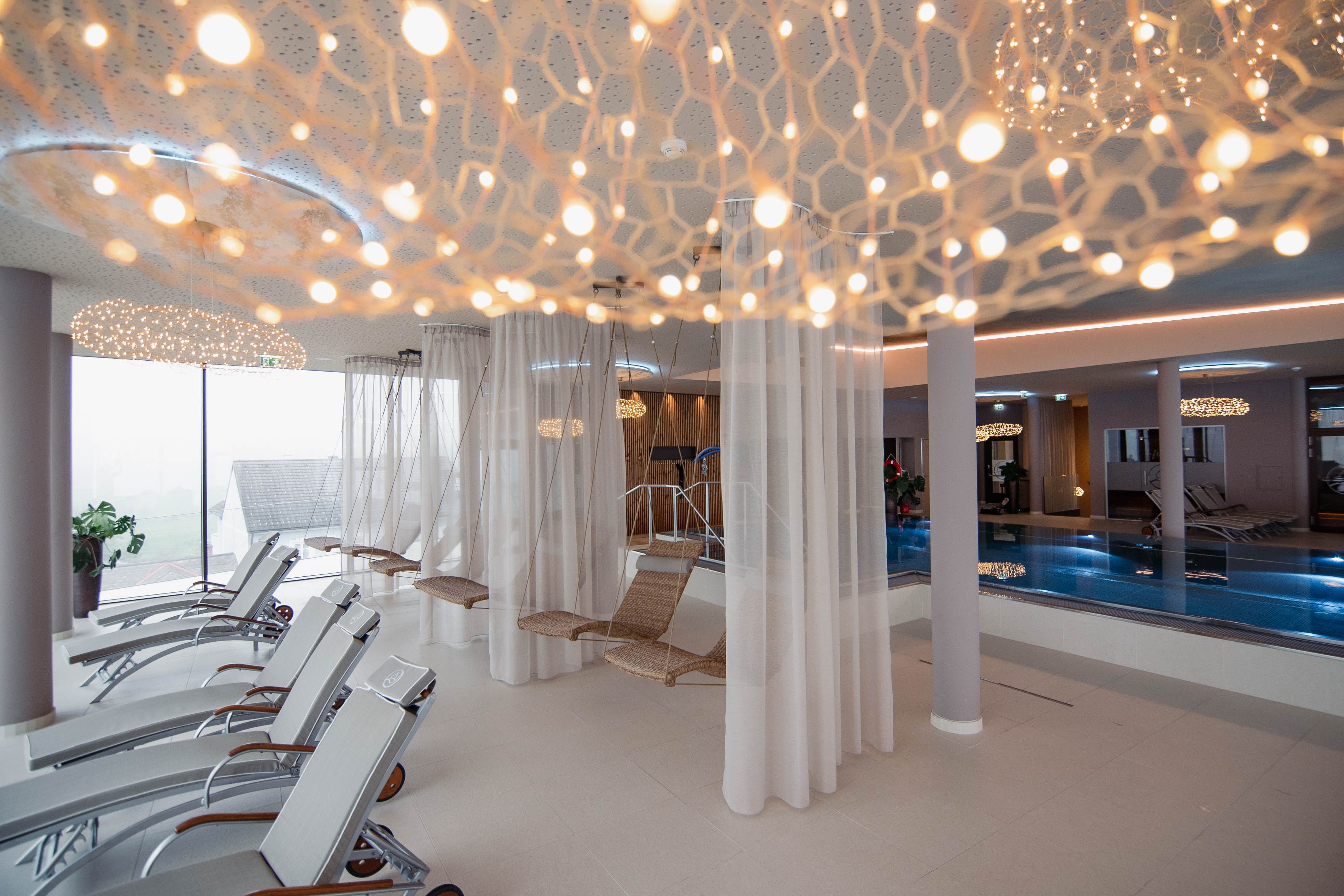 Modern spa relaxation area with loungers, hanging chairs and pool.