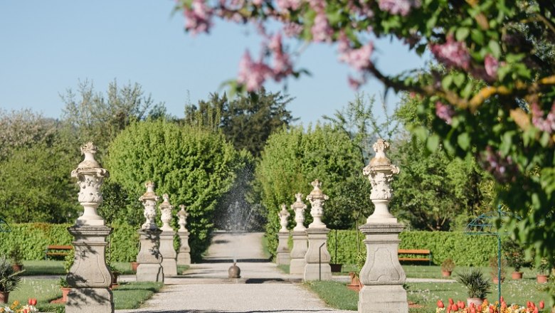 A well-kept garden path with statues and blossoming trees in spring.