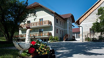 A farm with a green house, flowers and a goose statue in the foreground.