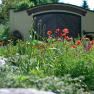 Blooming garden with red poppies in front of a building with a wooden gate.