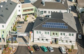 Aerial view of a building complex with the Gasthof zum Alten Brauhaus, solar panels on the roof and several parked cars.