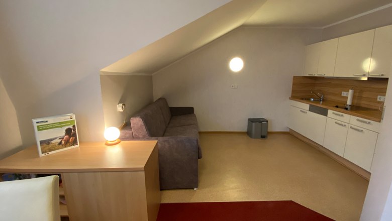 Interior view of a vacation apartment with sofa, table lamp and kitchenette.