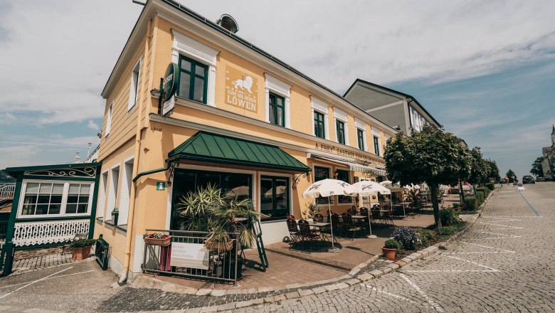 Exterior view of a yellow inn with terrace and parasols.