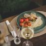 A plate of grilled gilthead bream fillet, lemon risotto and cherry tomatoes, served on a wooden table with a glass of white wine.