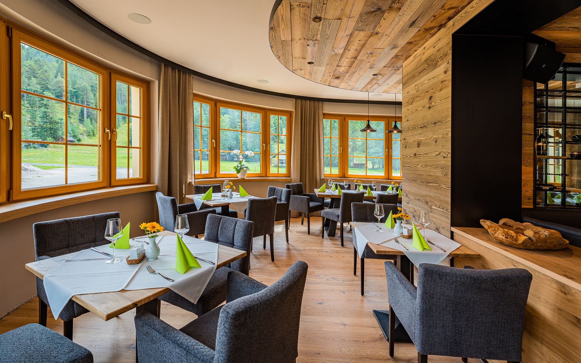 Elegant restaurant with wooden elements, laid tables and large windows overlooking the greenery.
