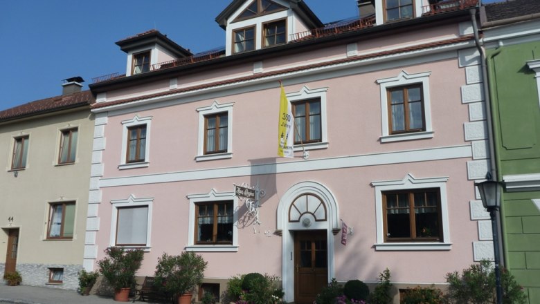 Exterior view of a pink house with white window frames and a yellow flag.