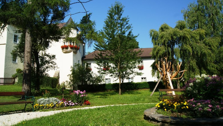 A castle with a white façade and red flowers, surrounded by a well-tended garden with trees and flowerbeds.