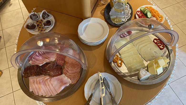 A breakfast buffet with cold cuts, cheese, vegetables, pastries and drinks on a table.