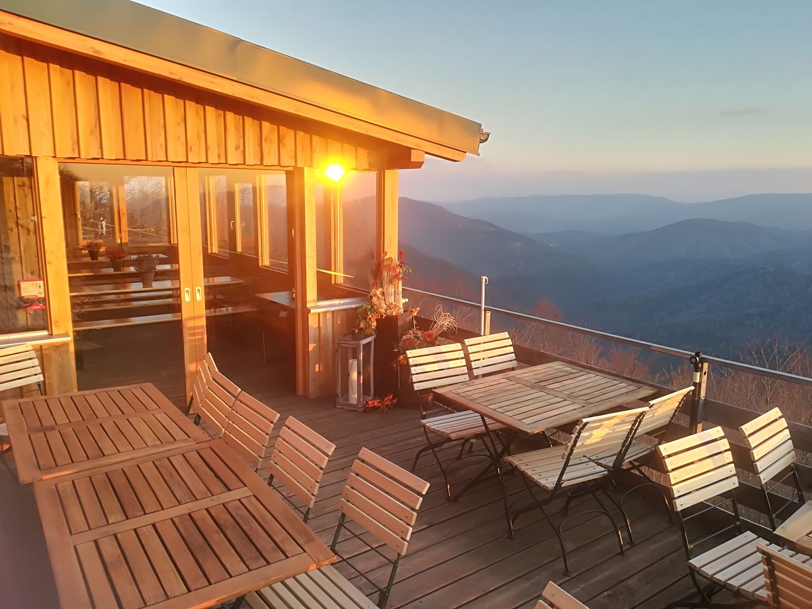 Terrace with wooden furniture and mountain views at sunset.