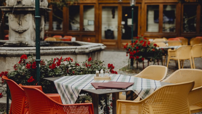 A guest garden with colorful chairs, a table with a tablecloth and a fountain in the background.