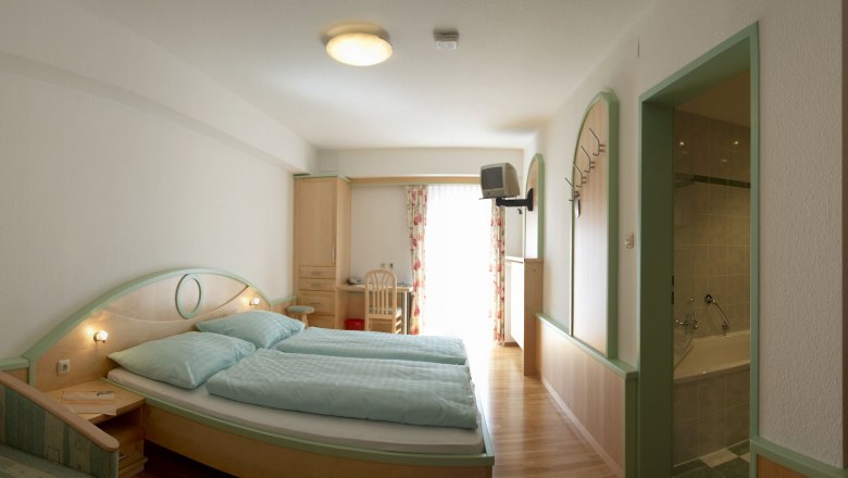 A hotel room with double bed, desk, TV and bathroom.