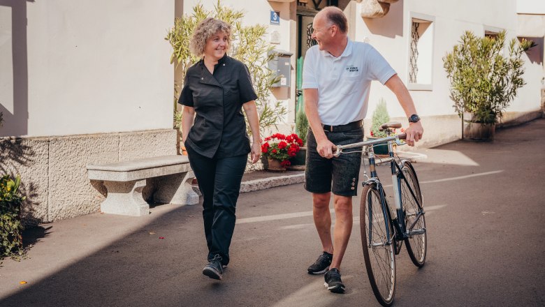 Two people are talking while one pushes a bicycle.
