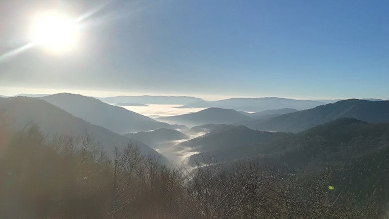 View from a mountain of mist-covered valleys and hills under a bright blue sky with sunshine.