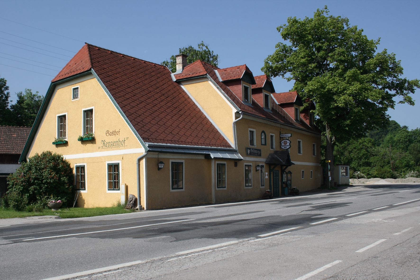 Yellow inn with a red roof on a road, surrounded by trees.