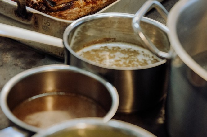 Roast in a casserole dish with pots on a stove in the kitchen.