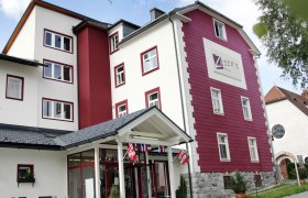 Exterior view of a multi-storey building with a red and white fa&ccedil;ade, labeled "Zusers Pension".
