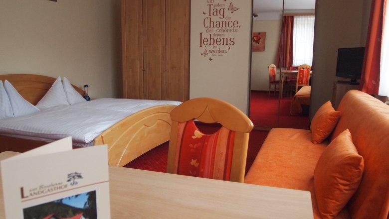 A cozy hotel room with a double bed, a sofa, a table and a wardrobe. There is a motivational slogan on the wall.