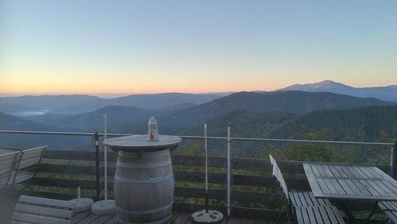 Terrace with wooden furniture and mountain views at sunrise.