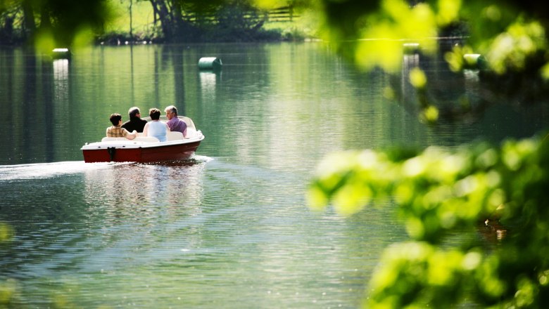 Four people in a boat on a calm lake, surrounded by green nature.