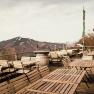 Empty terrace with wooden tables and chairs, mountain landscape in the background.